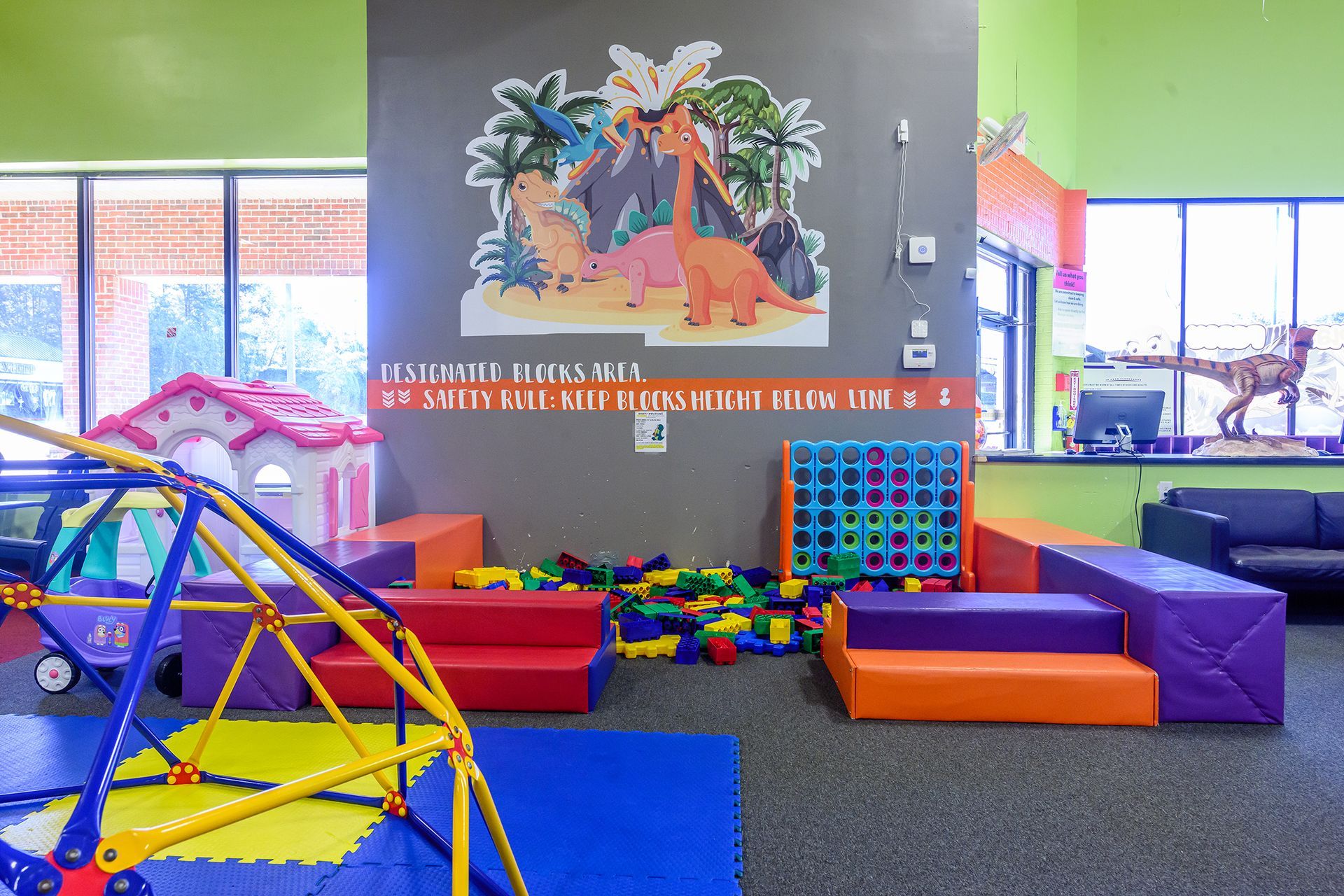 Indoor play area with dinosaur mural, soft blocks, and climbing structure.