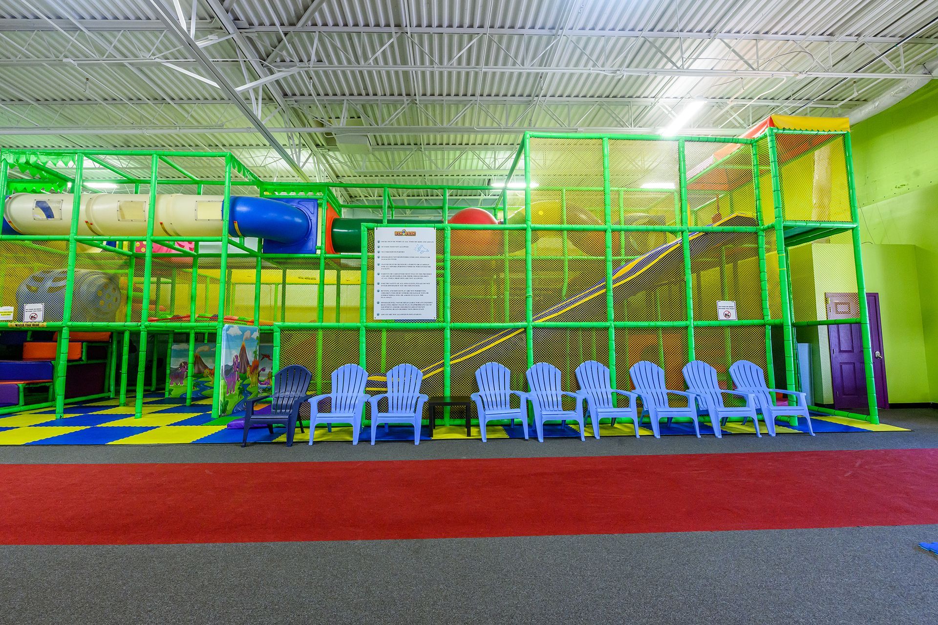 Indoor playground with green frame, tunnels, and chairs.