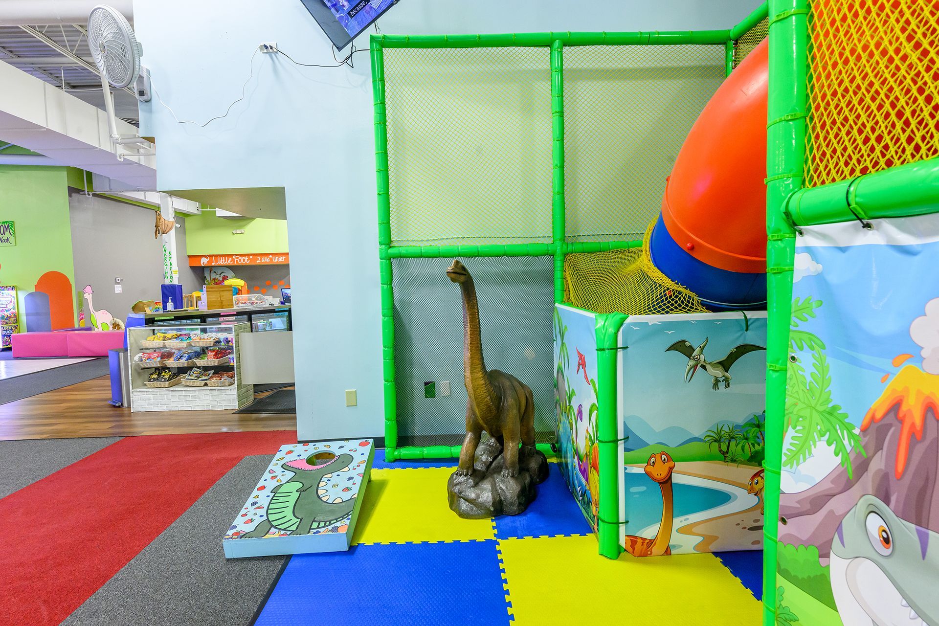 Indoor children's play area with a dinosaur theme, including a slide, climbing structure, and soft flooring.
