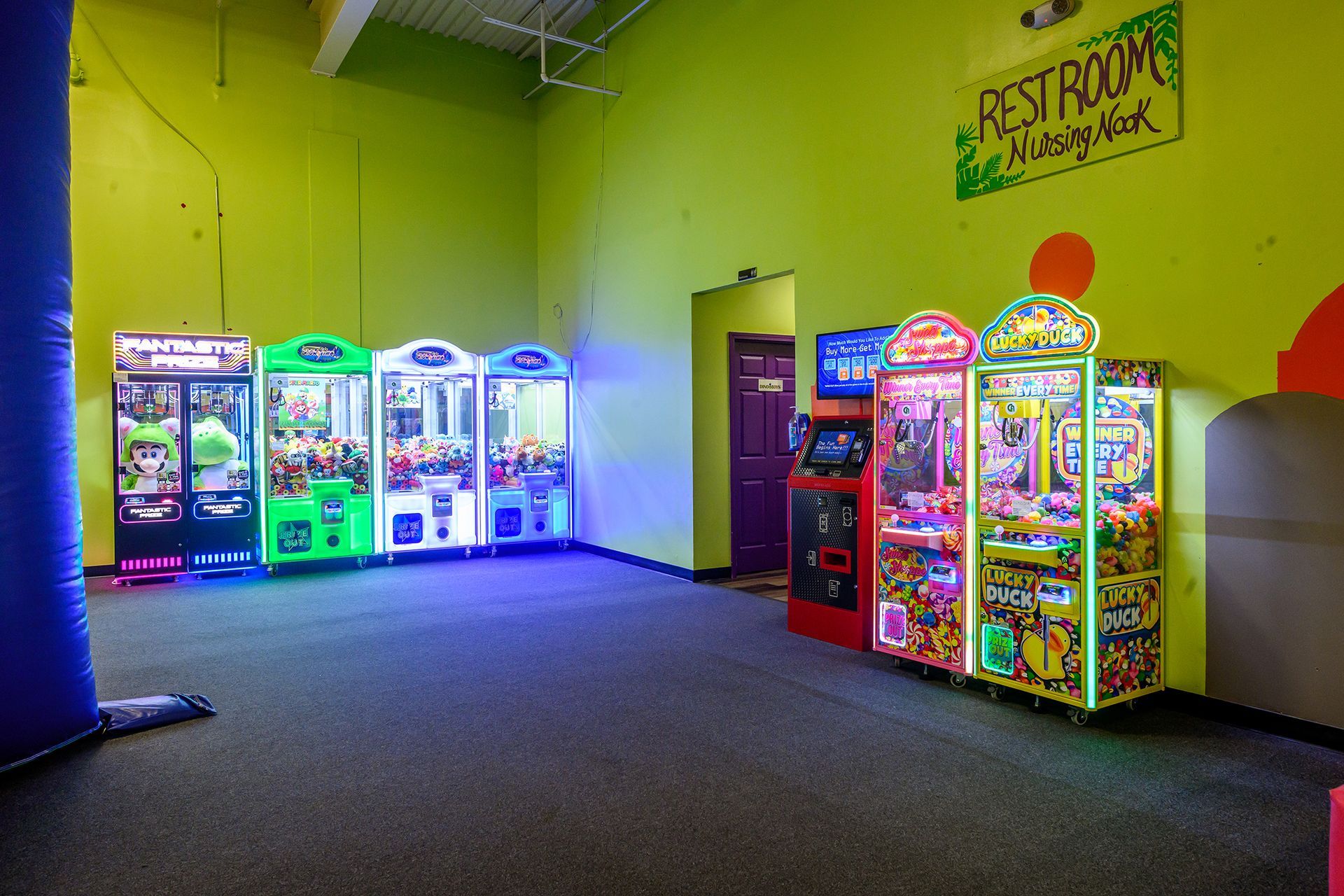 Arcade games against a bright green wall, with a door and restrooms sign.