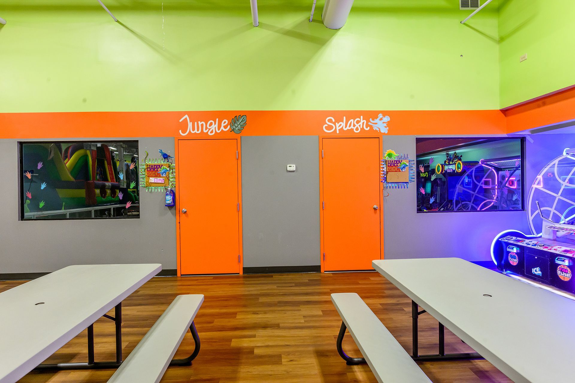 Party room with orange doors, white tables, and colorful murals. 