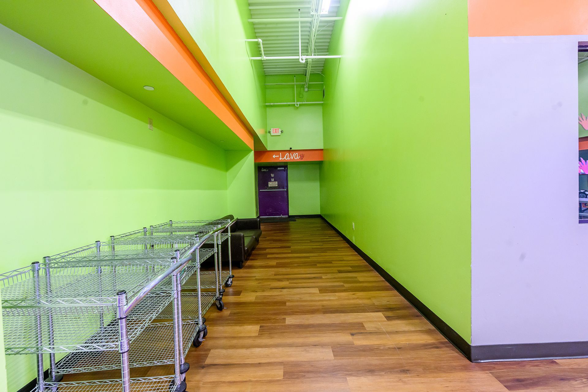 Green hallway with wood-look floor, metal shelves, purple door, and orange and green accents.