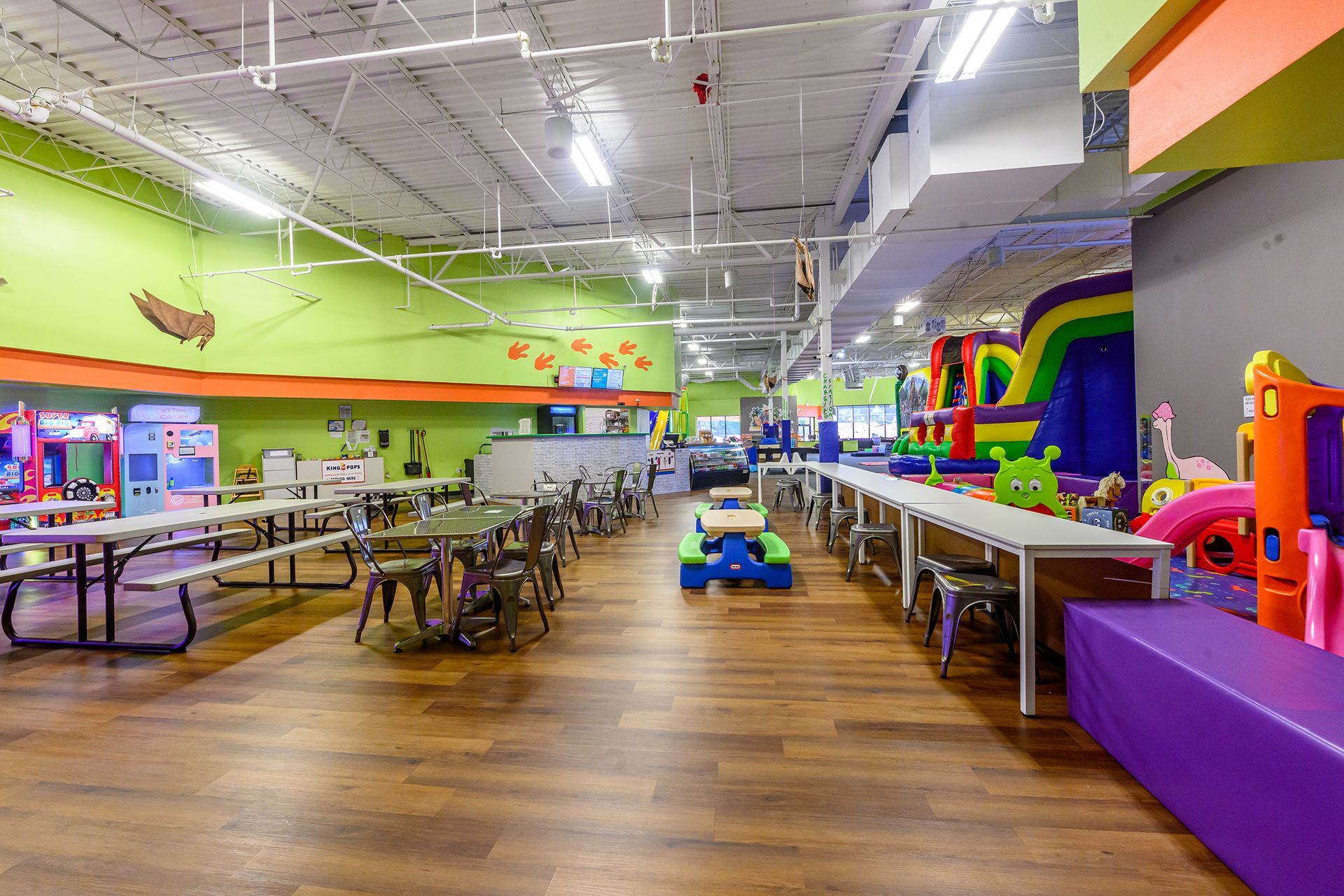 Indoor playground with tables, inflatables, and play structures on a wooden floor.