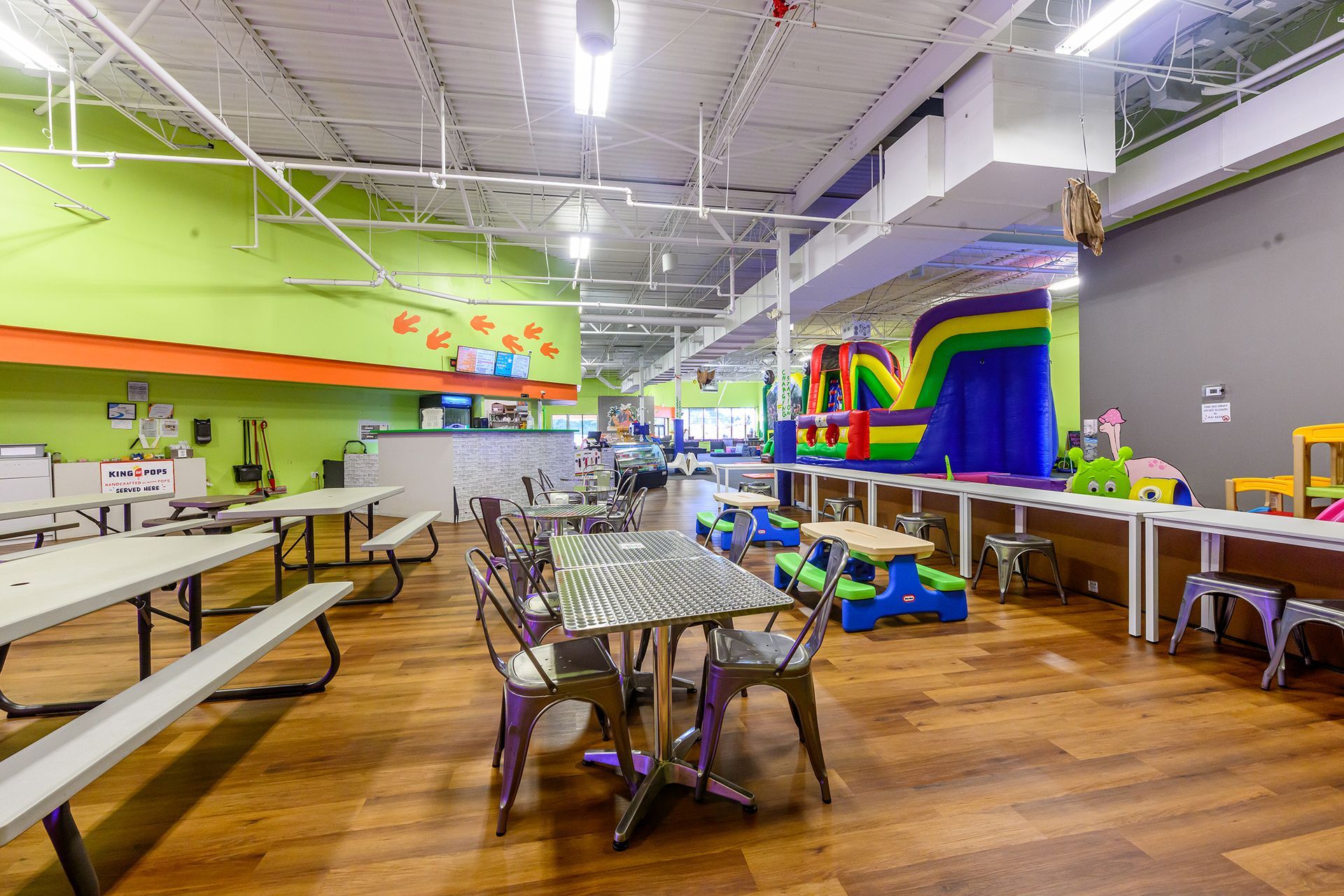 Indoor play space with tables, bouncy castle, and green and gray walls.