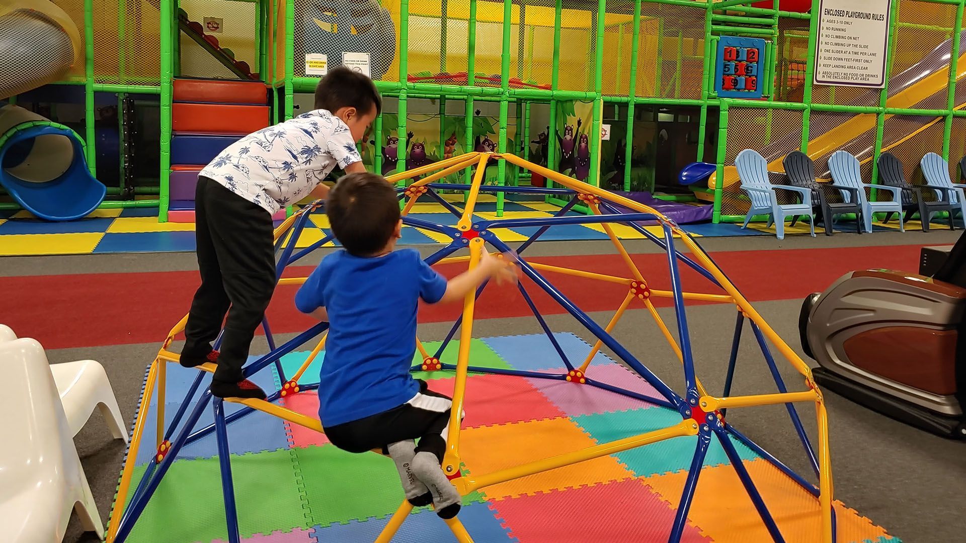 Two young boys are playing on a climbing dome in a playground.
