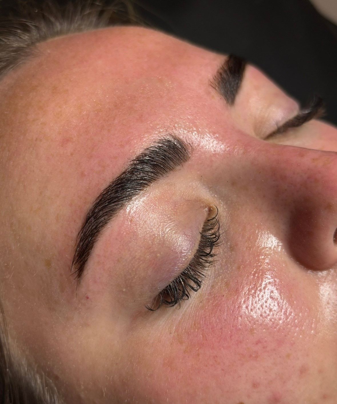 Close-up of a person's eye and eyebrow; dark, defined brow over closed eye, hydrated skin with a hint of redness.