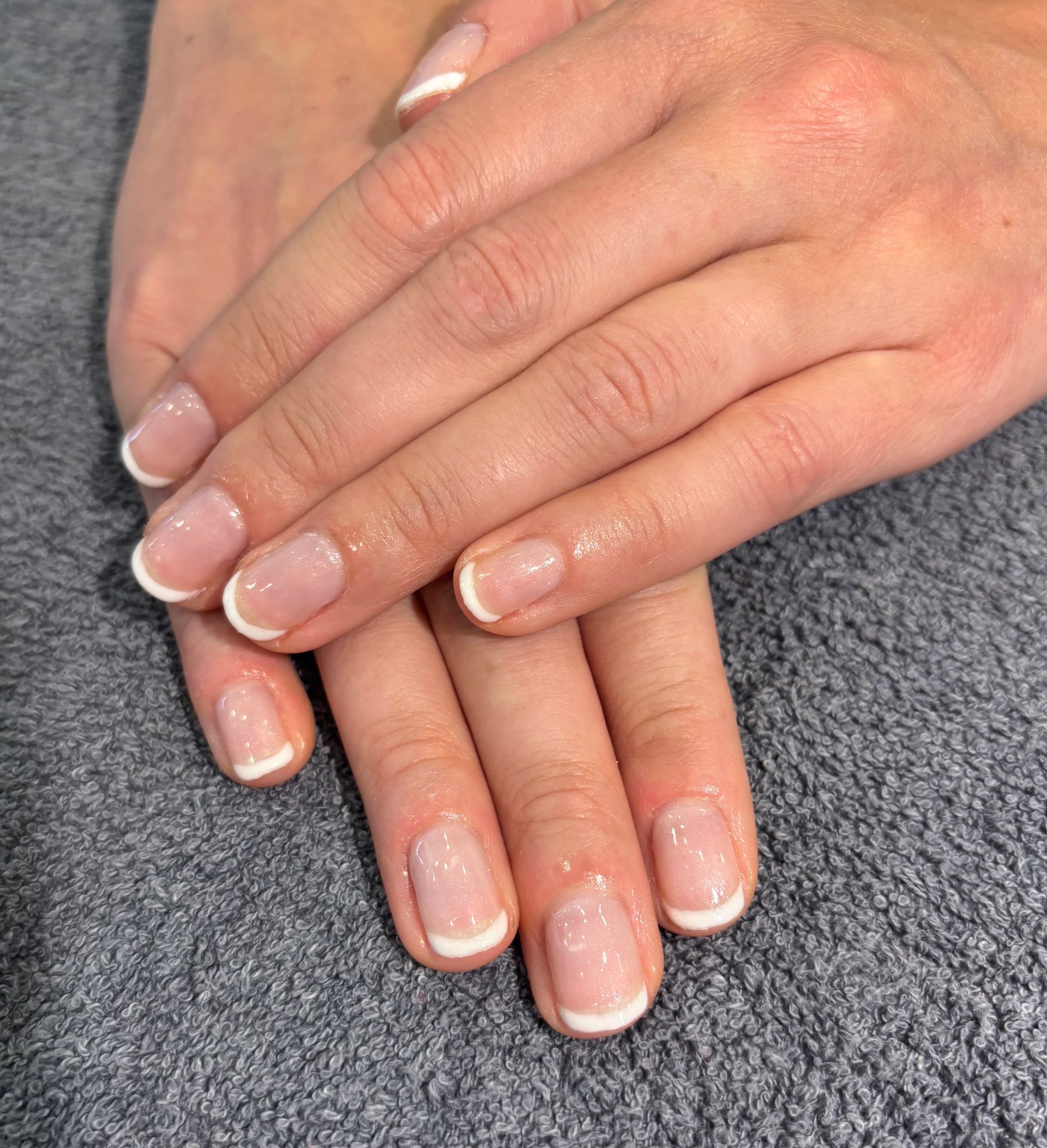 Hands with French-tip manicure. Light pink base with white tips. Nails are short.