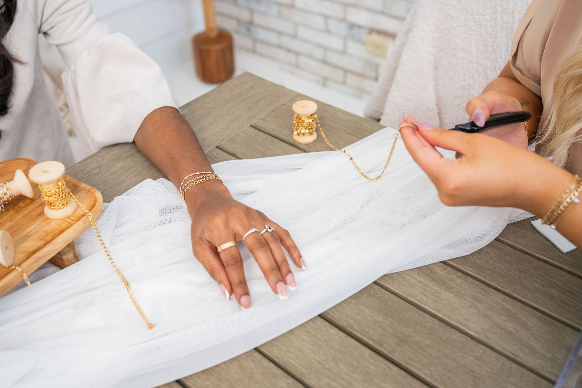 Person's hand with jewelry being adjusted by another's hand. Wooden table, spools of thread.