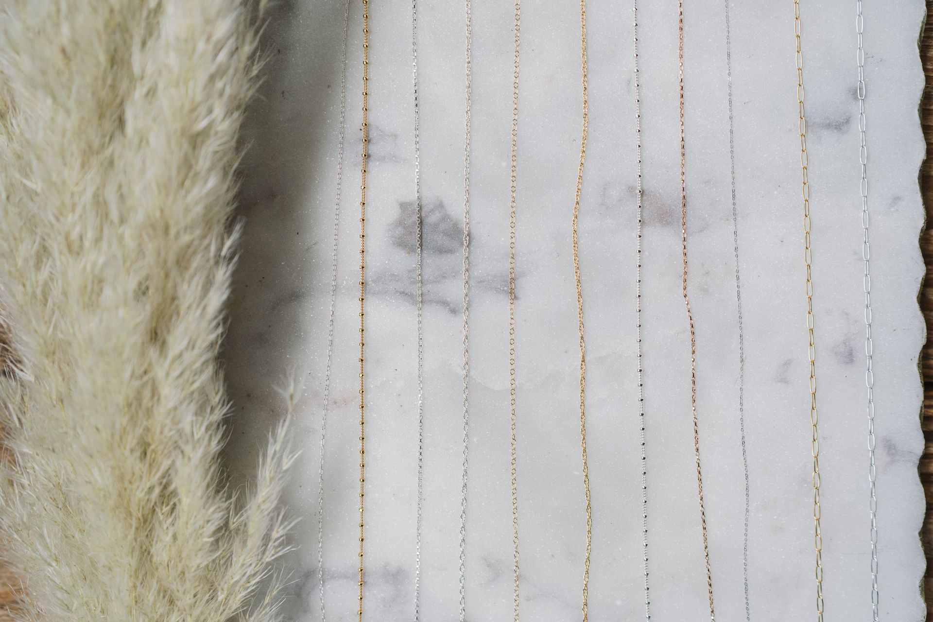 Pampas grass next to a white marble background with vertical gold and silver lines.