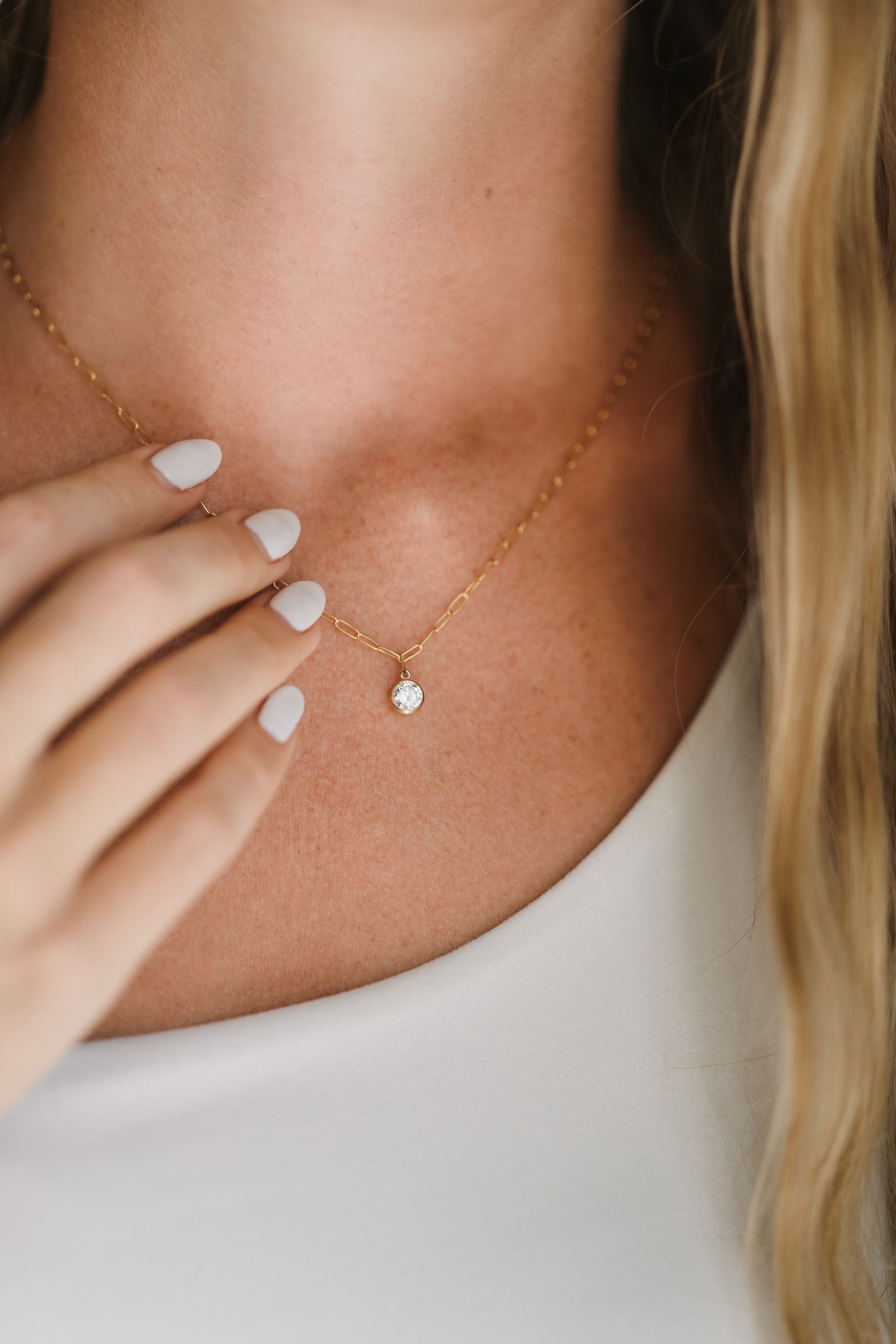 Gold necklace with a small pendant on a woman's neck, hand on chest.