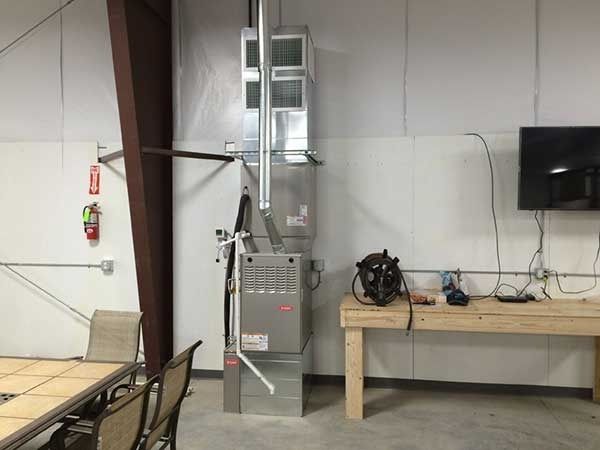 Furnace unit and ductwork in a room with a workbench, TV, and dining table.