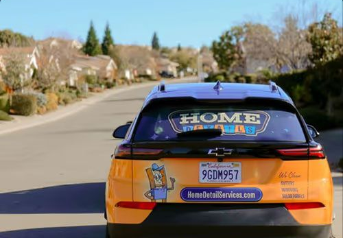 Orange-and-black advertising car driving on a suburban street, rear view.