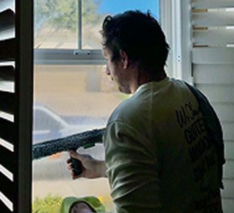 Person aiming a shotgun out an open window inside a house