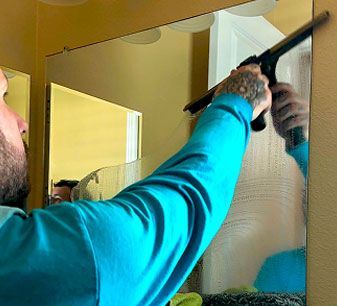 Person in a blue shirt reaching up to adjust a mirror in a bathroom