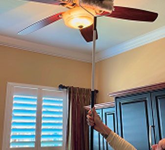 Hand lifting a pole to adjust a ceiling fan with a light in a room with windows and curtains