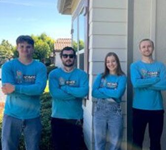 Four people in blue shirts stand with arms crossed outside a building.