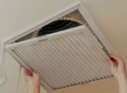 Hands removing a white ceiling vent cover from a beige ceiling opening