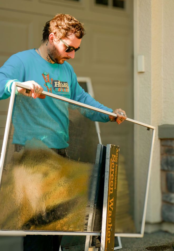 Man spraying paint on a framed panel outdoors with a roller