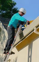 Person in a helmet uses a ladder to work on a roof under blue sky