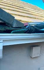 Close-up of a roof edge with shingles, white gutter, and a small wall-mounted box below the eaves