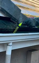 Yellow-and-black rope securing stacked dark roof tiles on a white gutter outside a house
