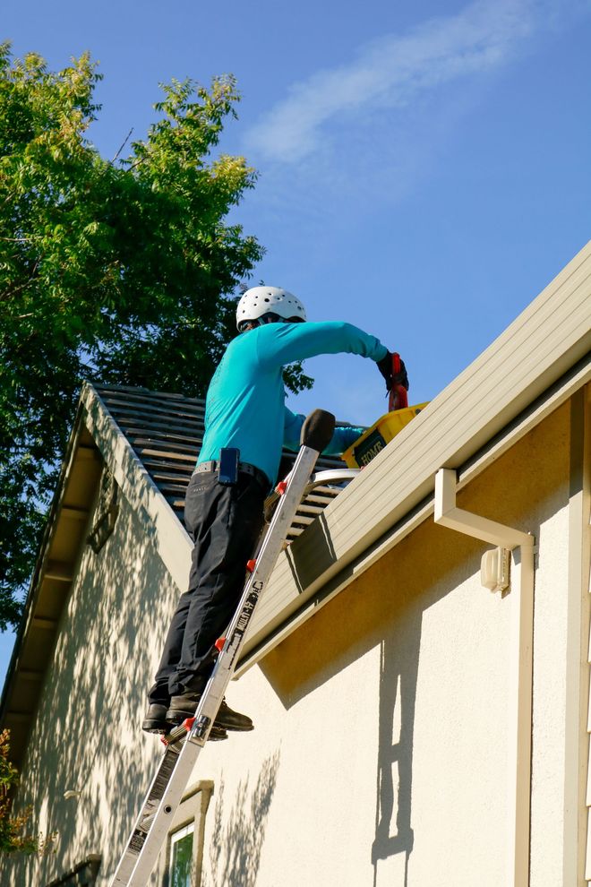 Person on a ladder painting the roof edge of a house with a roller