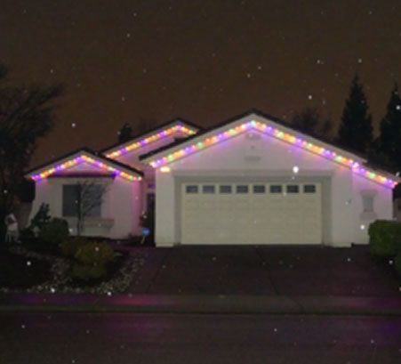 Suburban house at night with colorful Christmas lights along the roofline and garage.