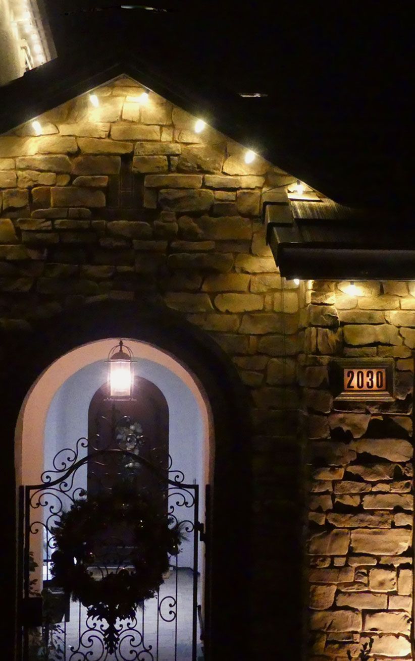 Stone house entrance at night, warmly lit doorway and roofline against a dark sky