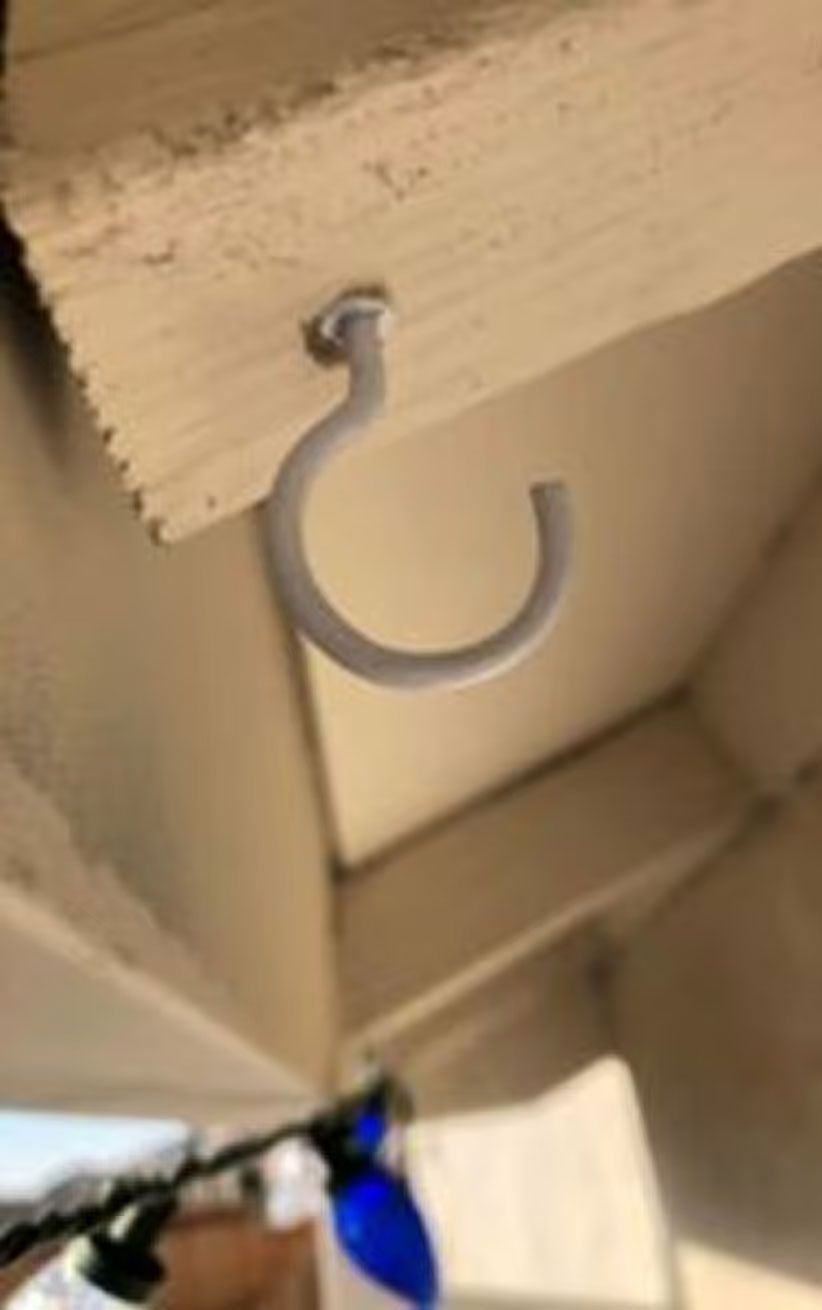 White metal hook hanging from a wooden beam in a beige indoor space.