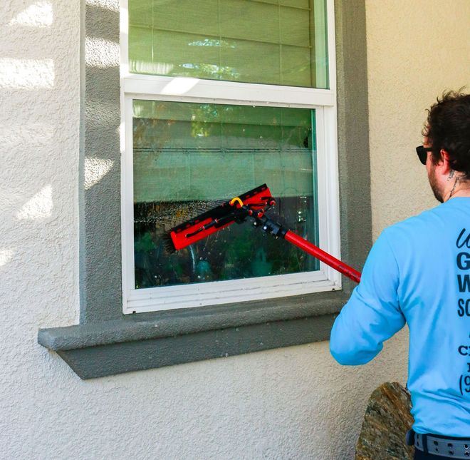 Person cleaning a window with a red squeegee on a house exterior