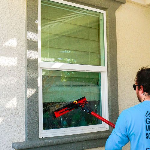 Worker cleaning an exterior window with a red squeegee
