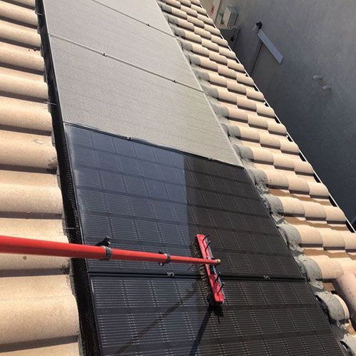 Solar panels being cleaned on a tiled roof with a red brush tool.