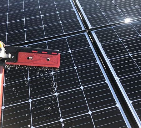Solar panels being cleaned with a red tool and water spray close-up