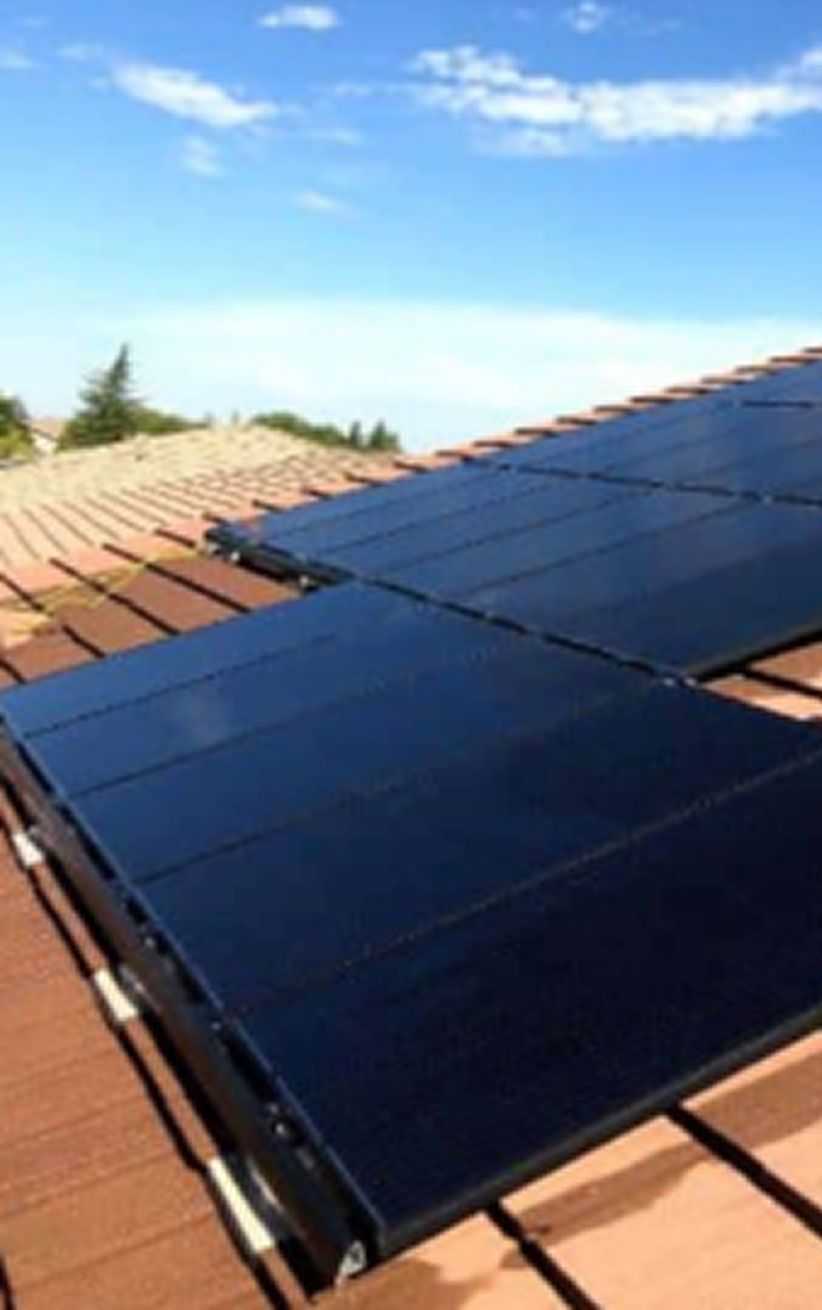 Dark solar panels installed on a terracotta tiled roof under a blue sky.