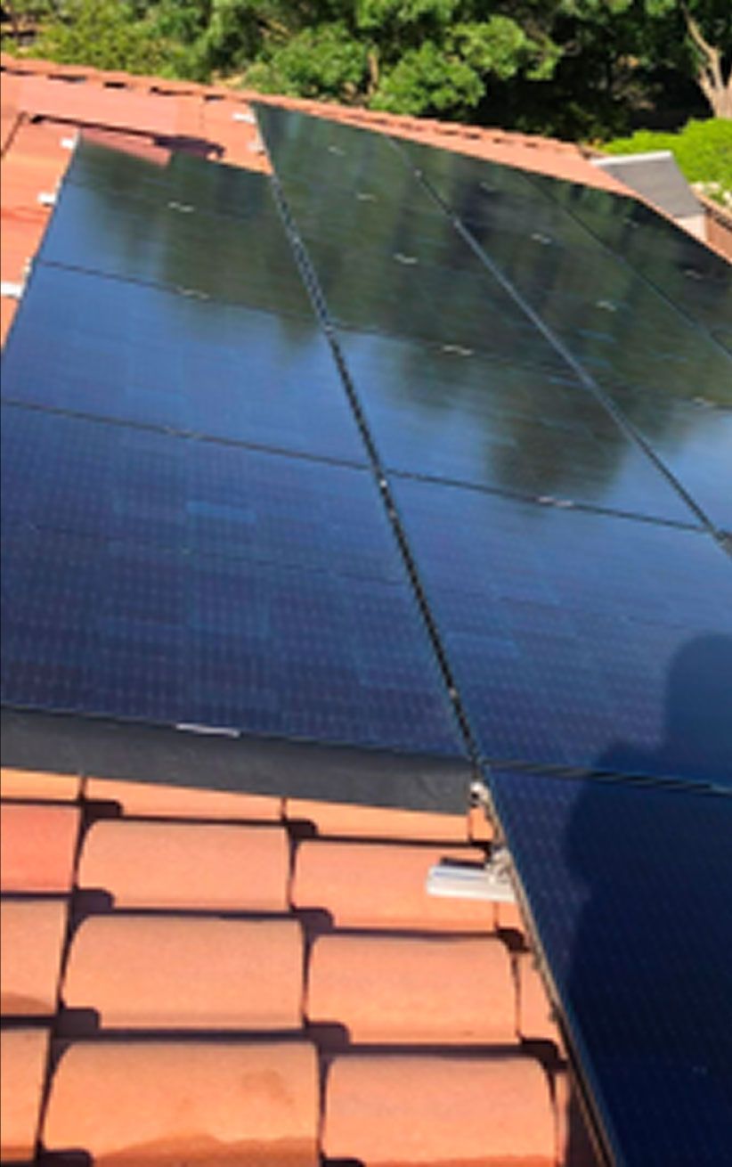 Solar panels installed on a red-tiled roof beside green trees in bright sunlight