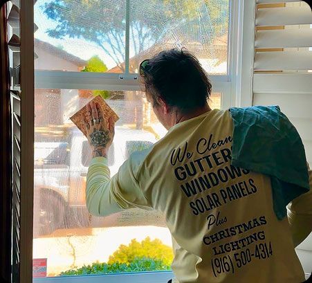 Worker cleaning a window with a cloth, wearing a white shirt with service text on the back.