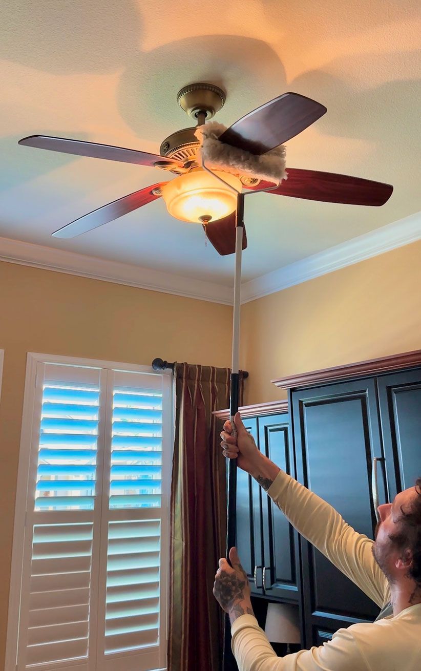 Person using a pole to adjust a ceiling fan in a room with shutters and curtains.