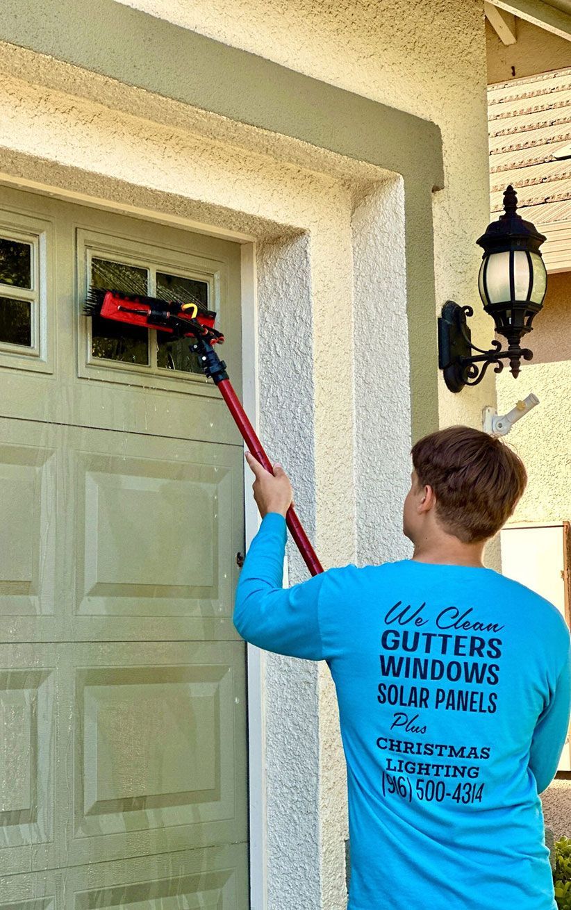 Window cleaner using a long red pole to wash an exterior window beside a garage door