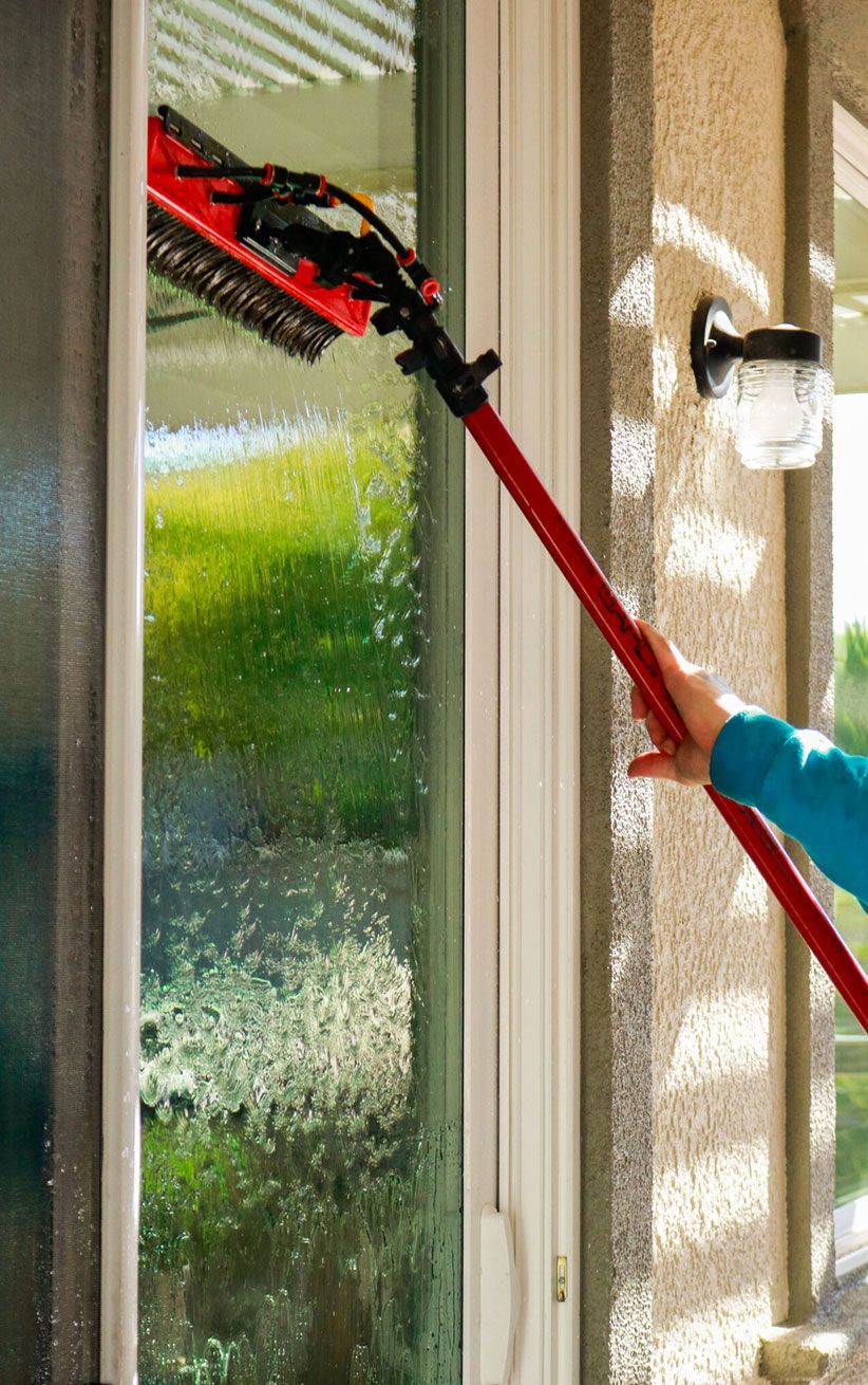 Person using a red extendable pole to clean a window on a house exterior