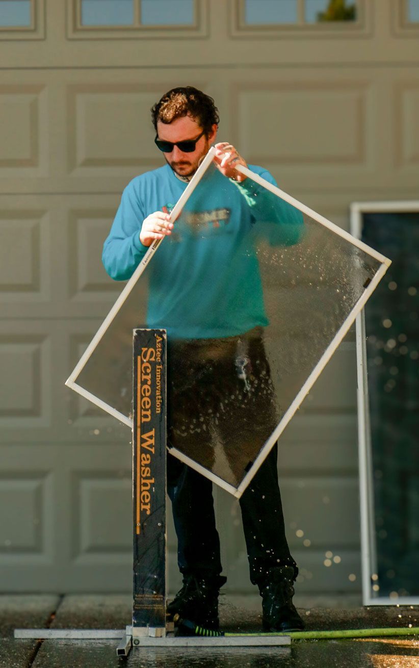 Man in sunglasses cleaning a large glass pane outdoors with a squeegee