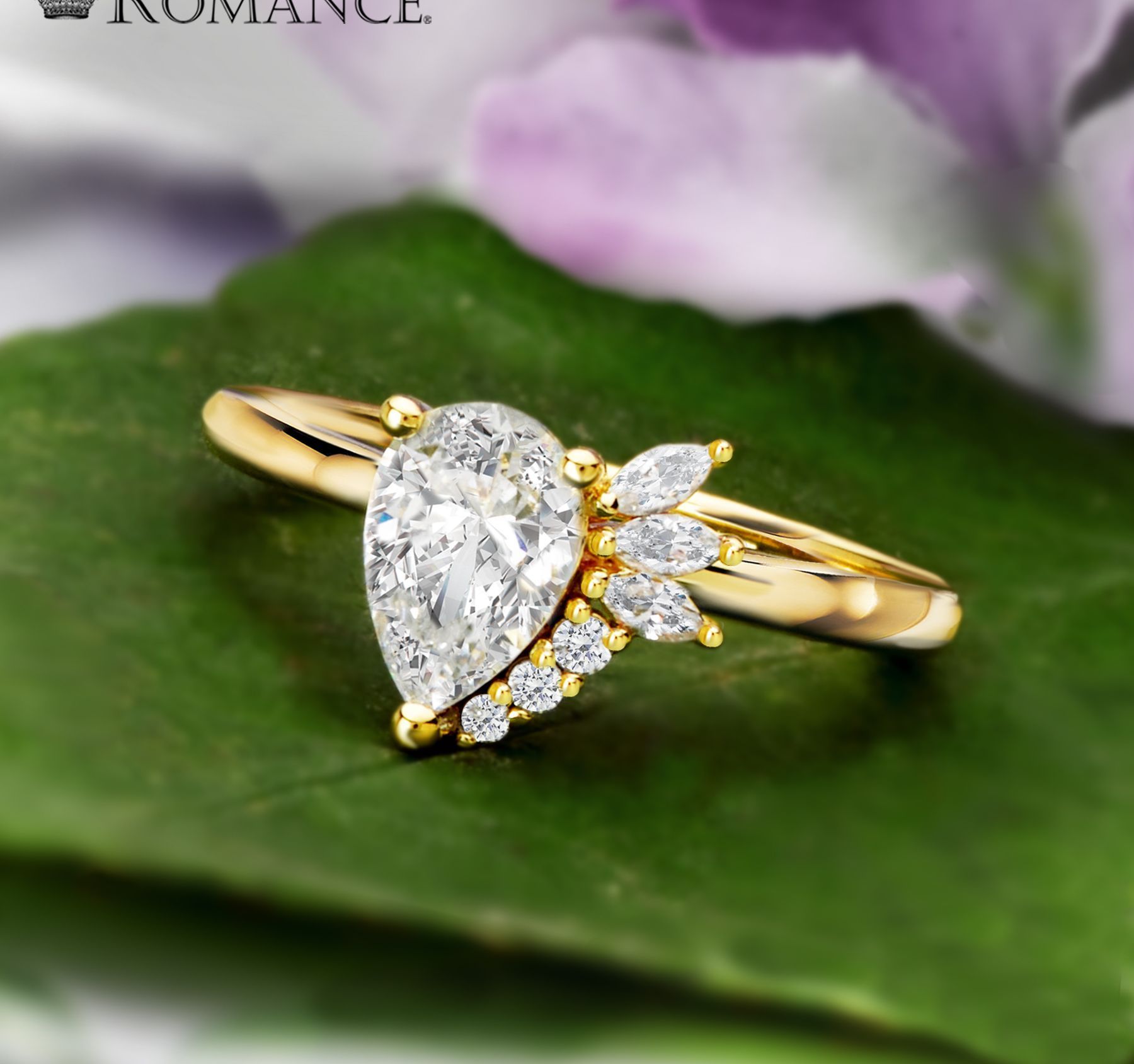 Gold engagement ring with a pear-shaped diamond and smaller accent stones on a green leaf.