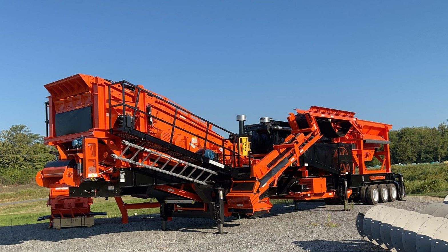 Orange industrial screening machine in a gravel lot under a clear blue sky
