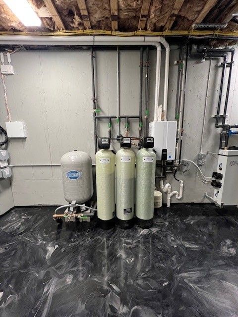 Water treatment system in a basement. Includes a pressure tank, three tanks, and piping along a white wall. 