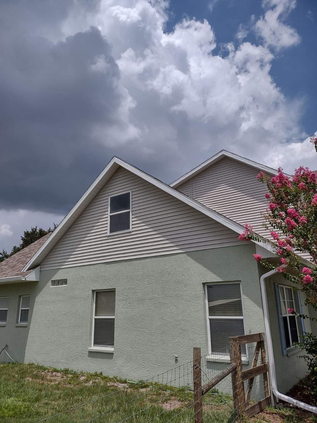 A white house with a brown roof and a wooden fence in front of it.