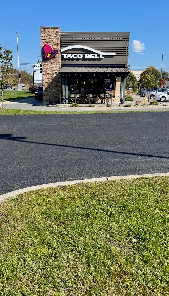 A Taco Bell restaurant is sitting on the side of the asphalt road next to a grassy area.