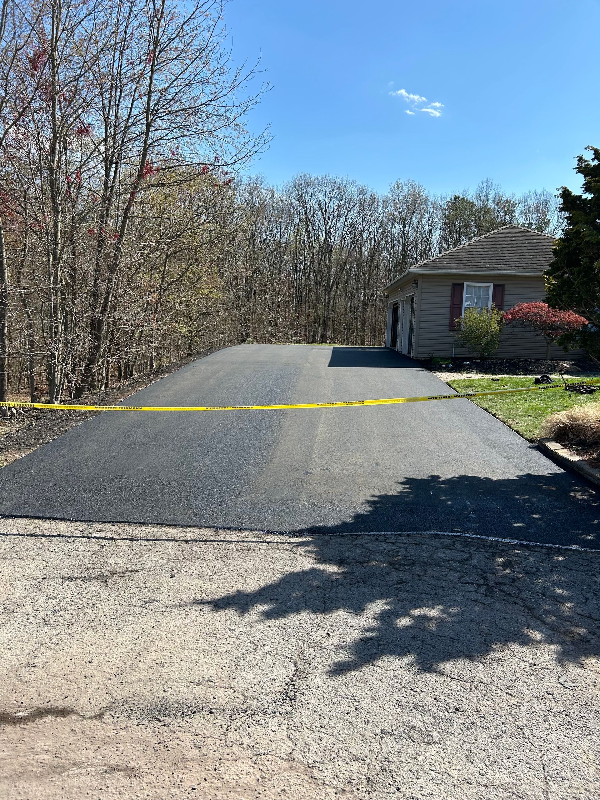 A newly paved driveway leading to a house with trees in the background.