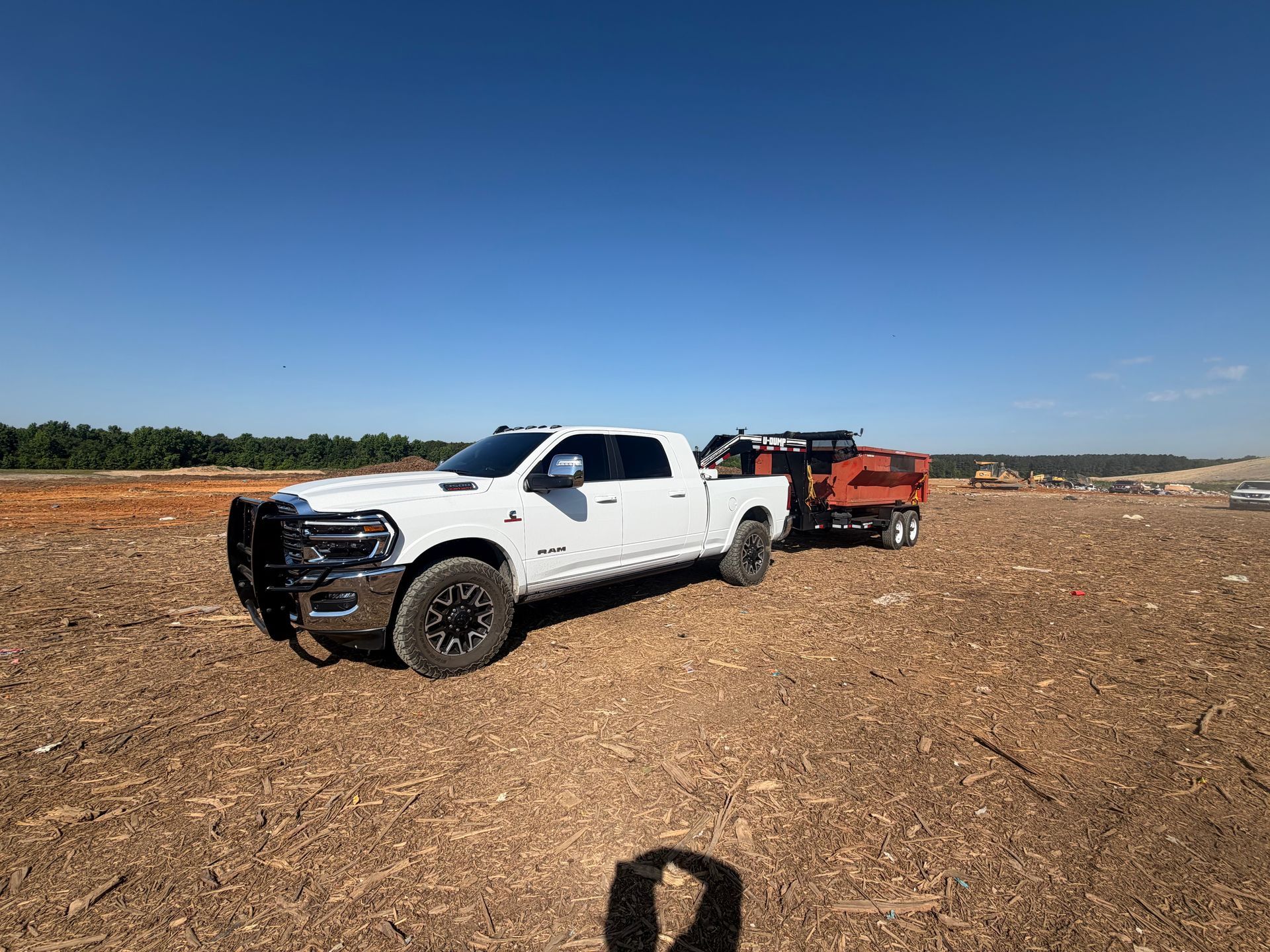 White pickup truck towing an orange trailer across a rocky dirt field under a clear blue sky