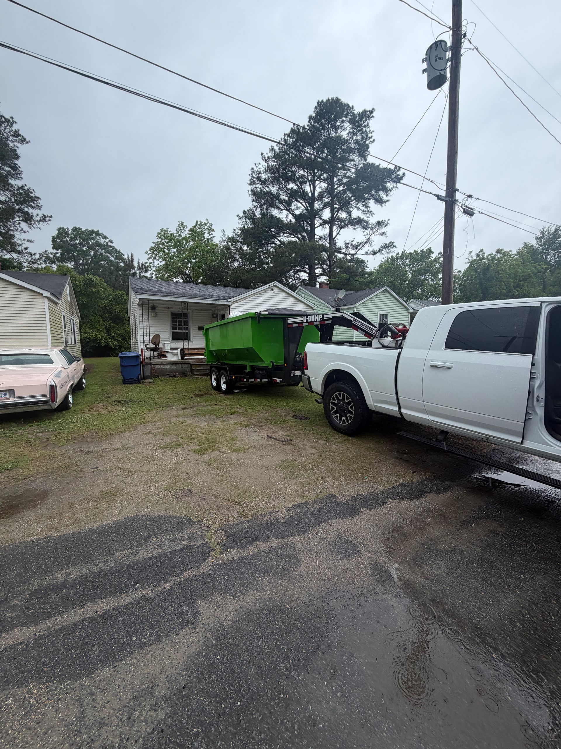 Gravel lot with white pickup trucks and a green utility trailer on a rainy day