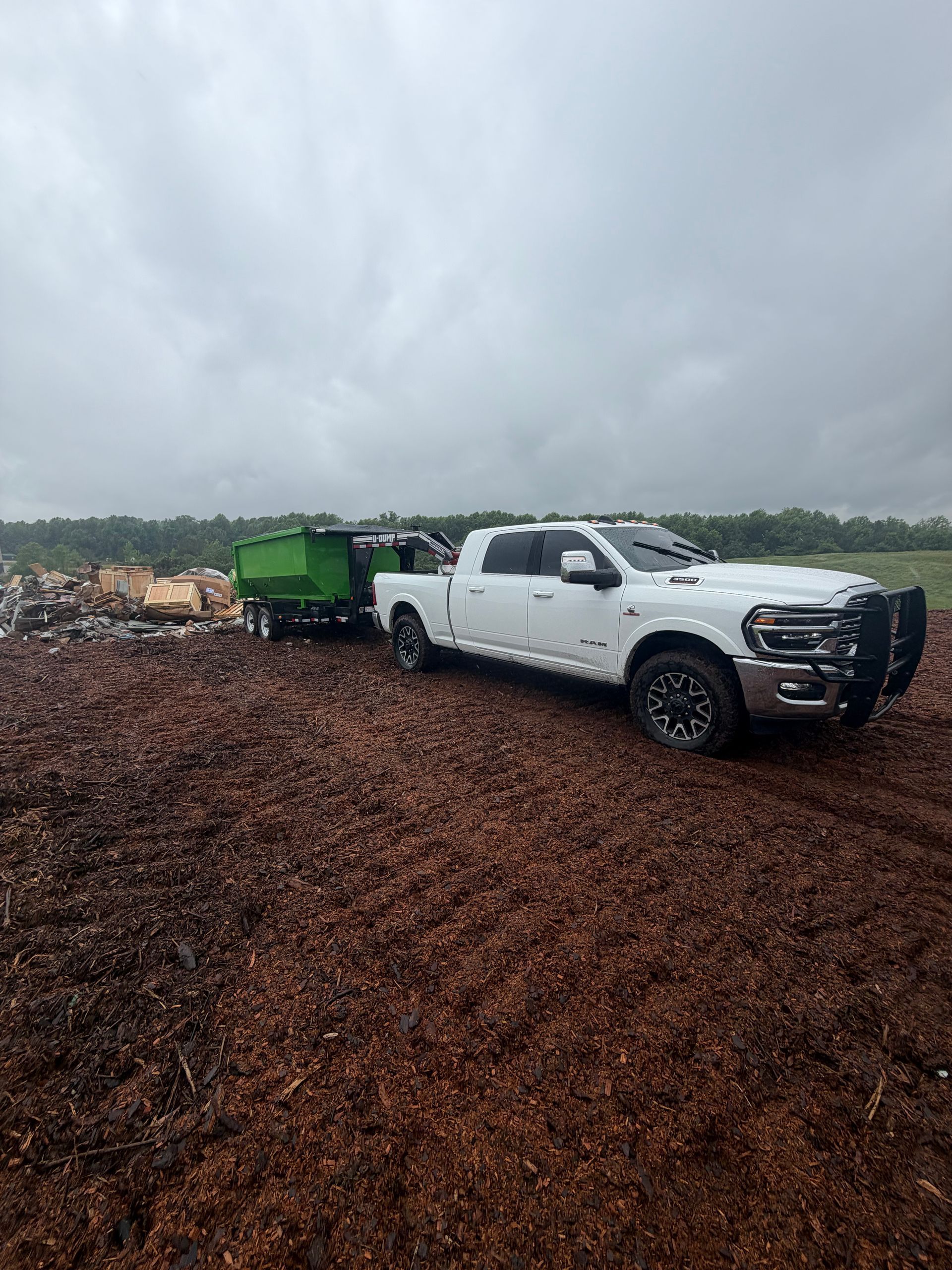 White pickup truck towing a green trailer on a muddy dirt road under cloudy skies