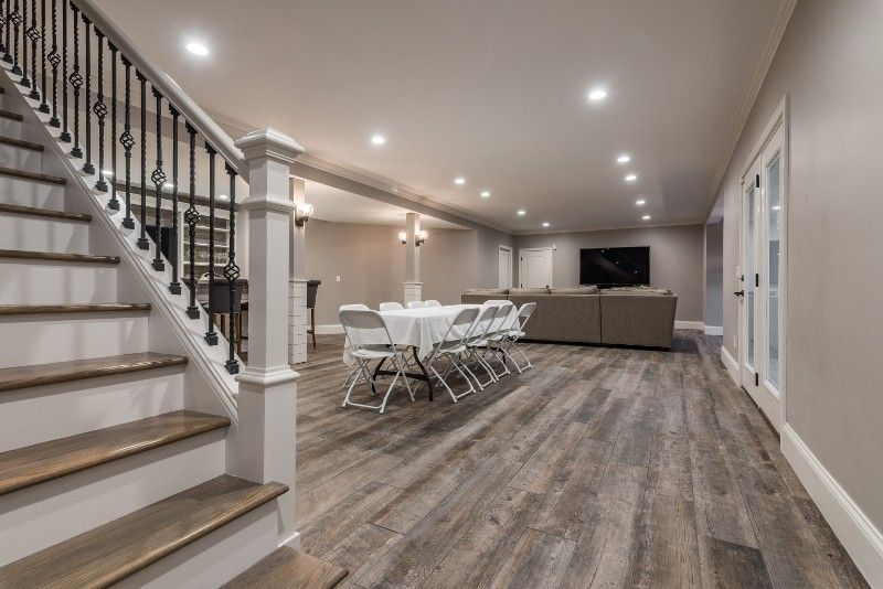 A basement with hardwood floors , stairs , a table and chairs.